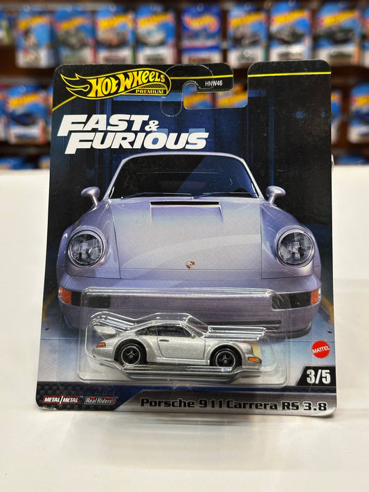 A Hot Wheels Premium die-cast model car of the Porsche 911 Carrera R5, shown in its original blister packaging. The packaging features a large graphic of a silver Porsche 911 and displays the small silver model car inside a clear plastic bubble.